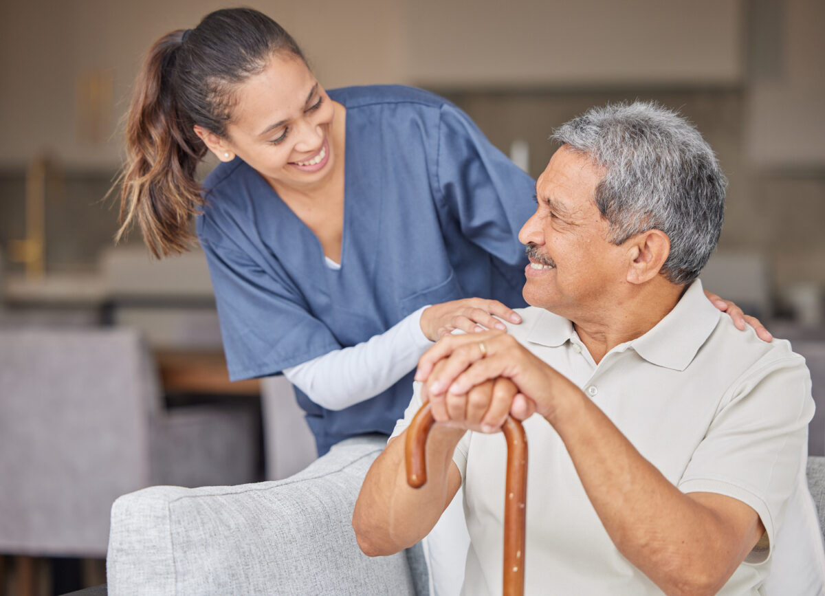 nurse smiling at male patient w a cane who is sitting in a chair