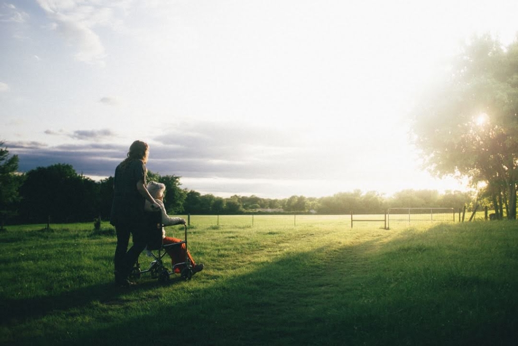 Woman pushing senior woman in wheelchair in field